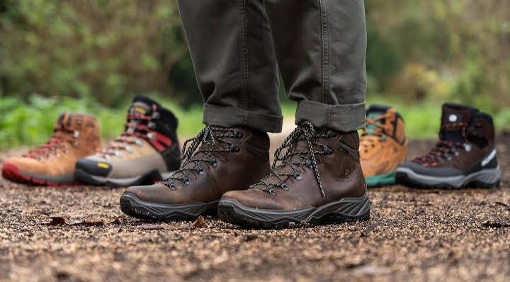 A walker standing on a gravel trail in broken in brown leather boots, with four more pairs lined up behind